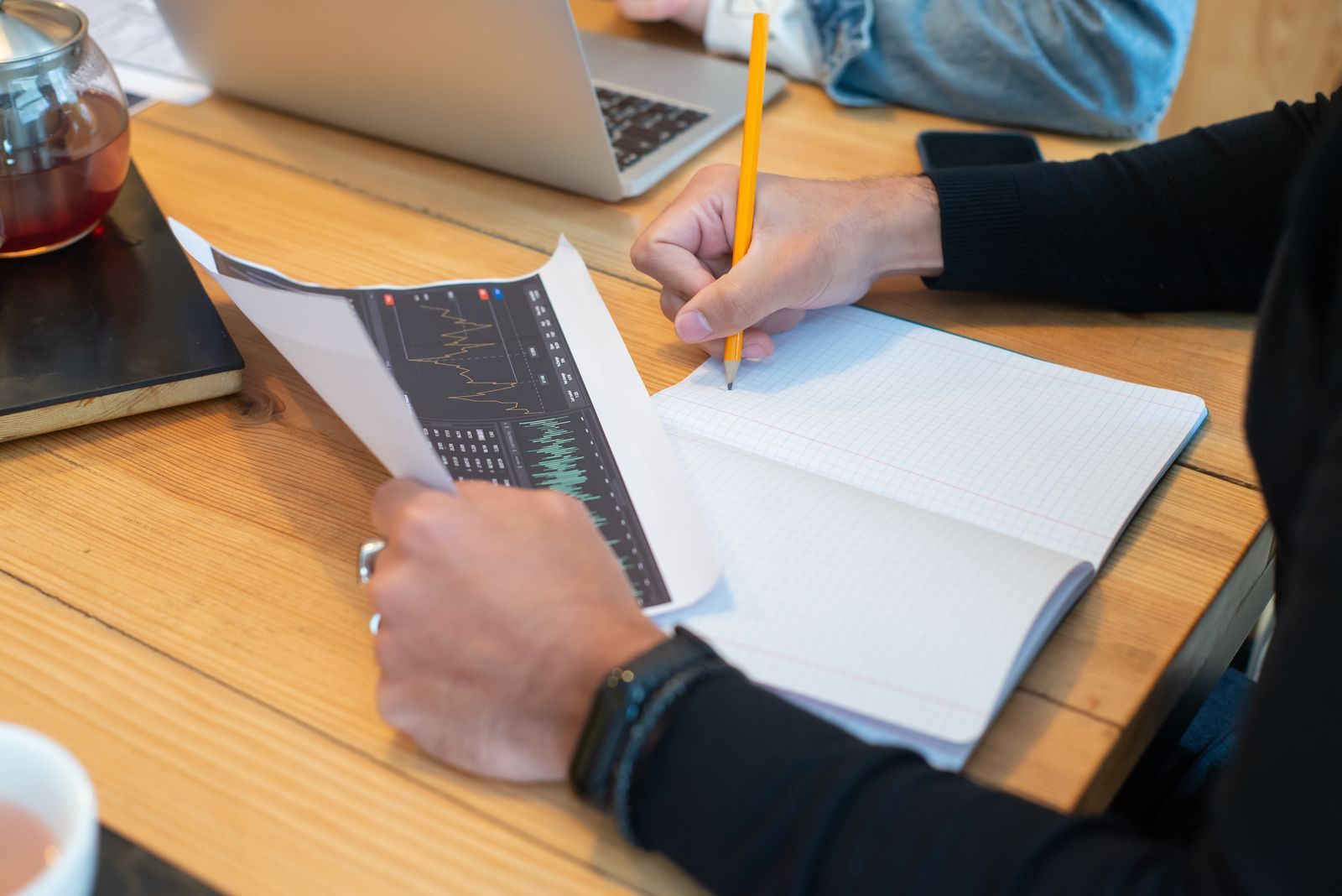 Hands writing meeting notes in a notebook next to a laptop during a business meeting